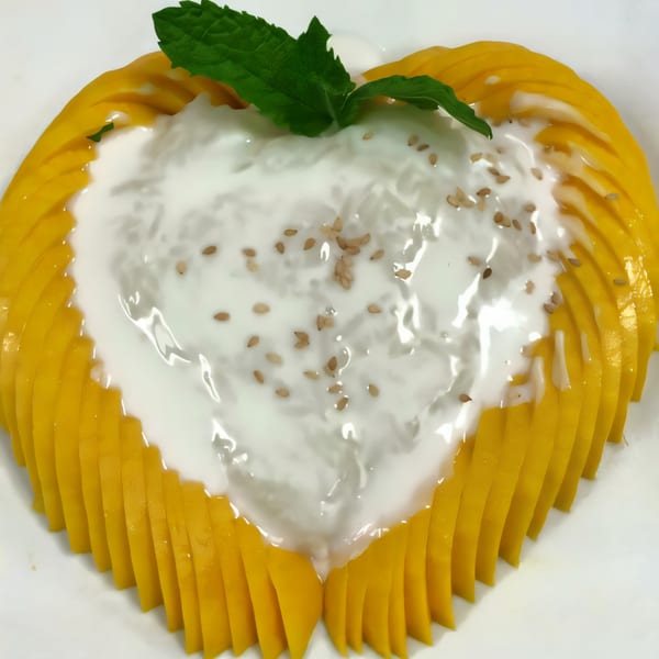 Heart-shaped mango sticky rice with coconut milk, sesame seeds, and mint garnish.