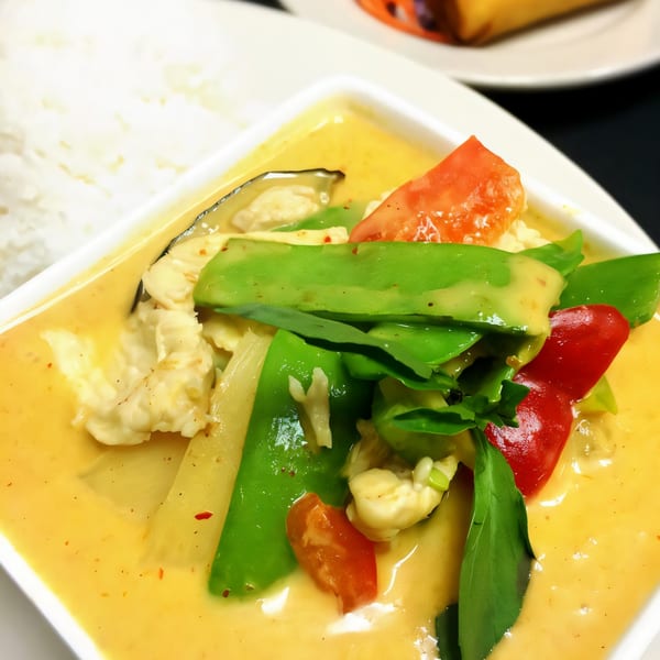 Close-up of a vibrant yellow Thai curry with chicken, green beans, red peppers, and basil, served with white rice.