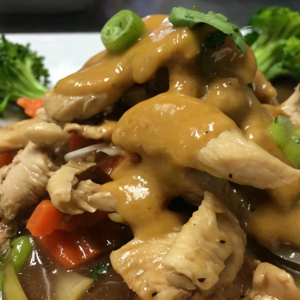Close-up of Thai chicken with peanut sauce, garnished with green onions and cilantro, with broccoli.