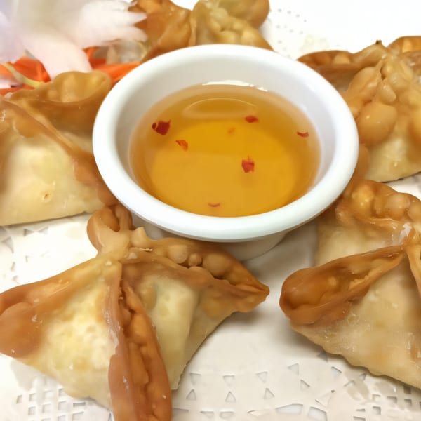 Golden fried Thai wontons arranged around a small white bowl of sweet chili dipping sauce.